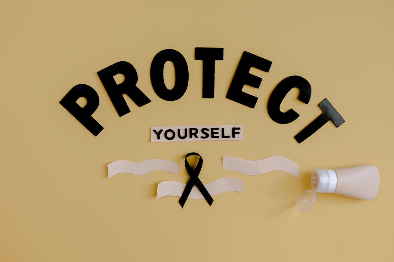 Black ribbon and lotion with 'Protect Yourself' on a yellow background representing health awareness.